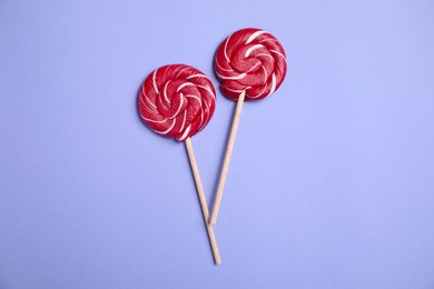 Sticks with bright lollipops on violet background, flat lay