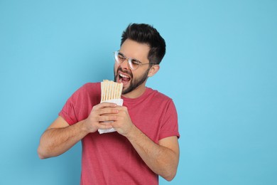 Photo of Young man eating tasty shawarma on turquoise background