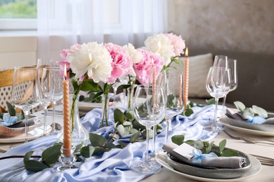 Photo of Beautiful table setting. Plates near glasses, peonies, burning candles and cutlery on table in room