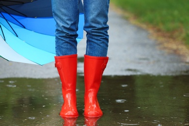 Photo of Woman with umbrella and rubber boots in puddle, closeup. Rainy weather