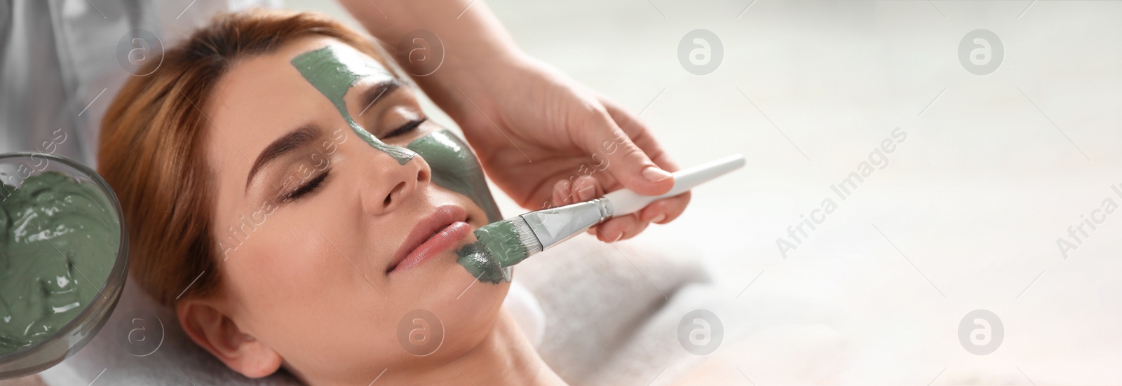 Image of Cosmetologist applying mask onto woman's face in spa salon, space for text. Banner design