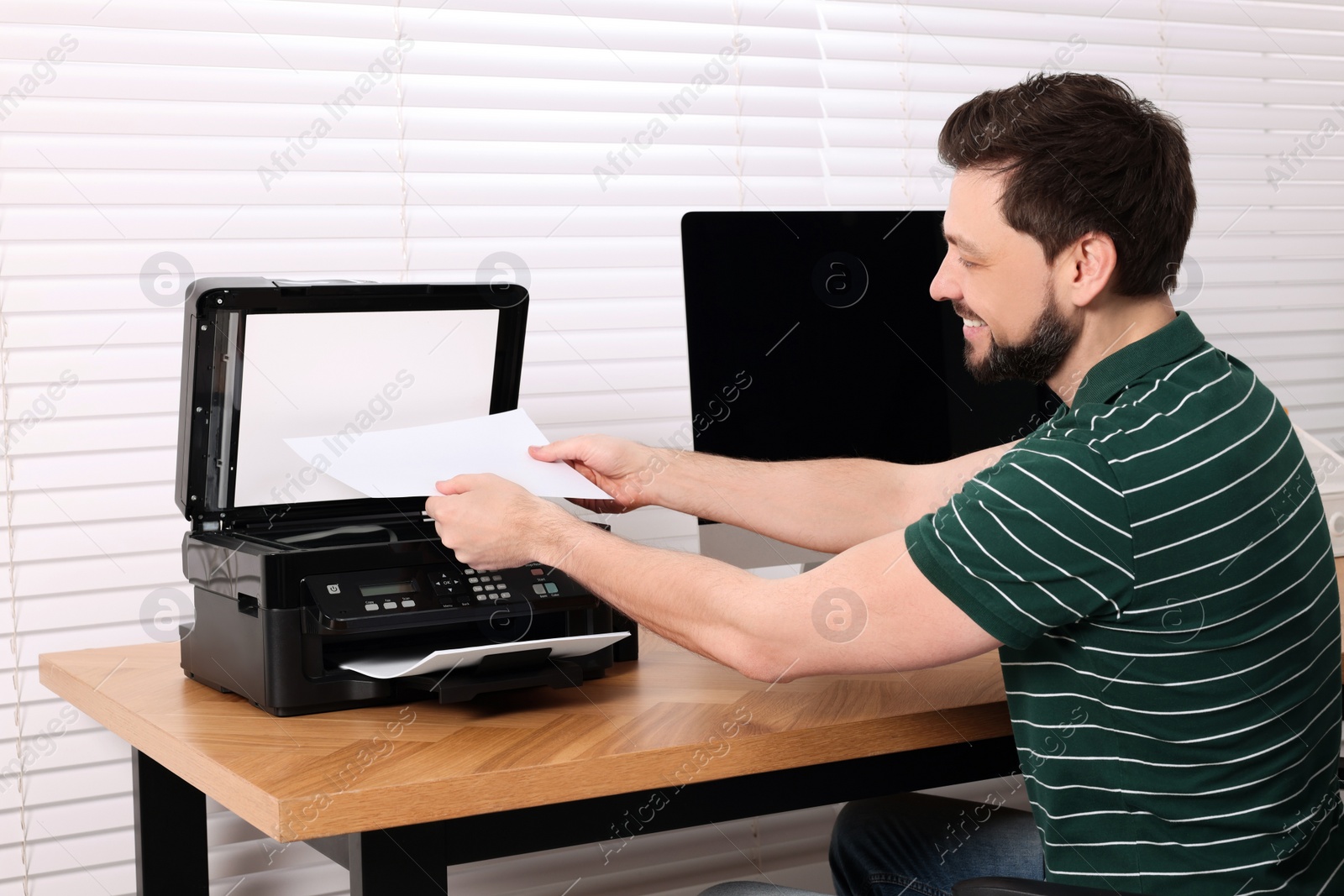 Photo of Man using modern printer at wooden table indoors