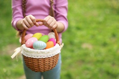 Photo of Easter celebration. Little girl holding basket with painted eggs outdoors, closeup. Space for text