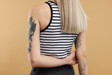 Photo of Woman with cool tattoos on beige background, closeup