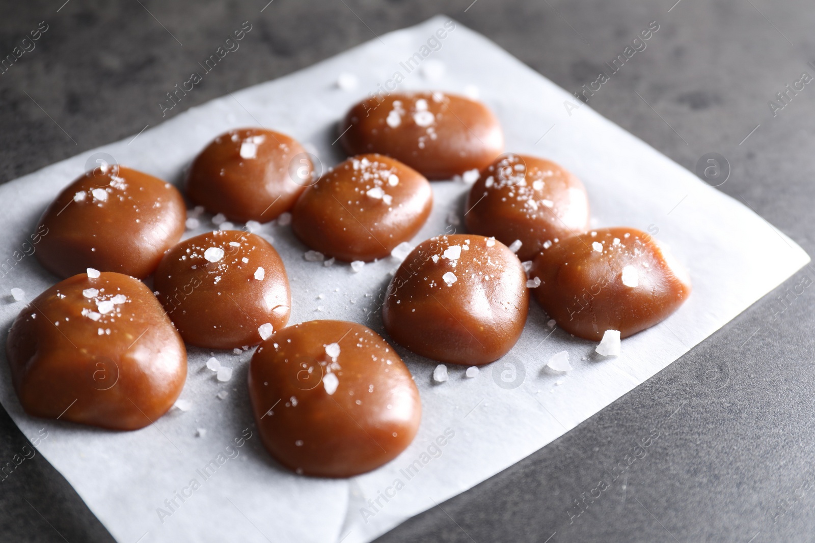 Photo of Tasty caramel candies and salt on grey table, closeup