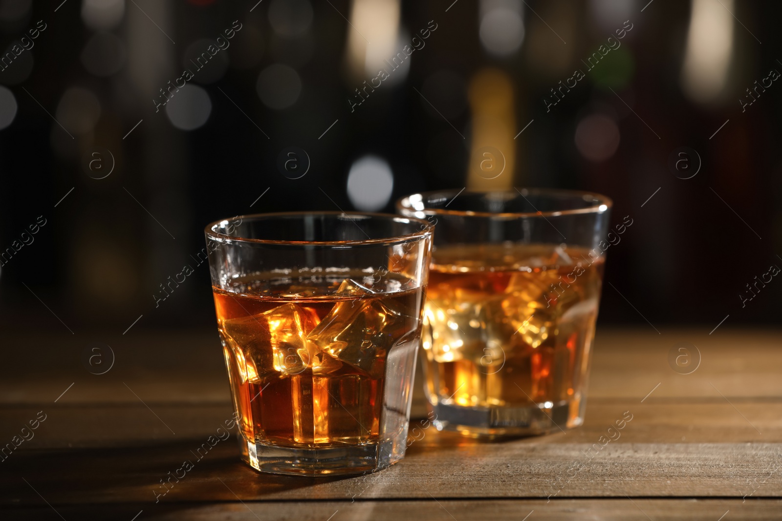 Photo of Glasses of whiskey with ice on wooden table in bar, space for text