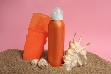 Sand with sunscreens and seashells against pink background. Sun protection care