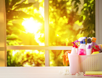 Image of Plastic basket with different detergents on wooden table indoors, space for text. Spring cleaning concept 