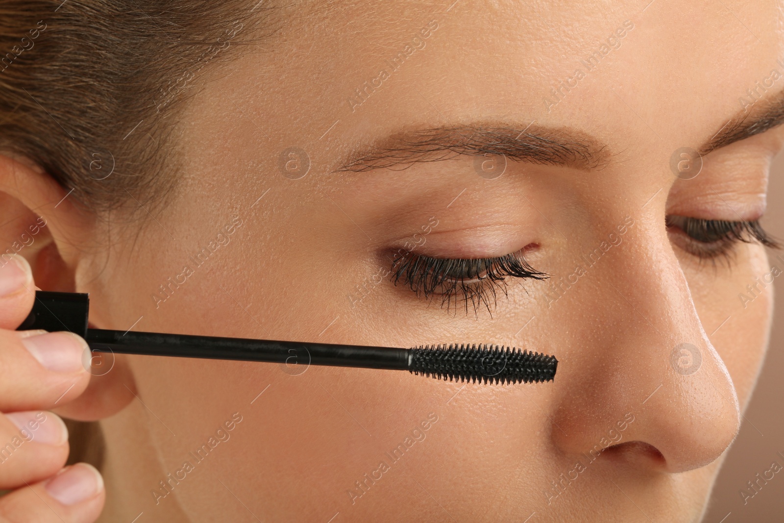 Photo of Woman applying mascara onto eyelashes, closeup view