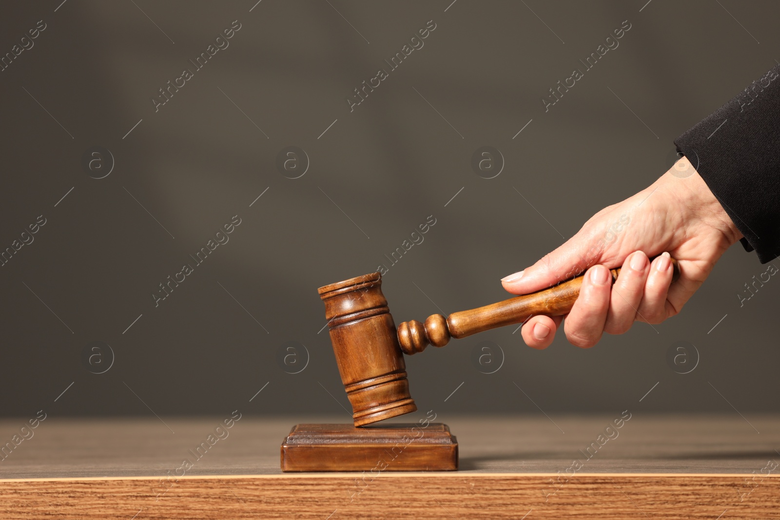 Photo of Judge striking mallet at wooden table against grey background, closeup. Space for text