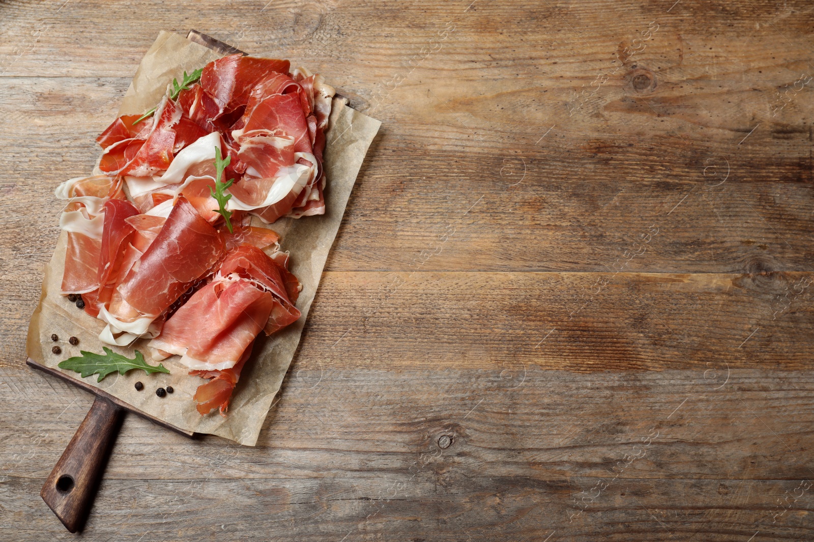 Photo of Pile of tasty prosciutto on wooden table, top view. Space for text