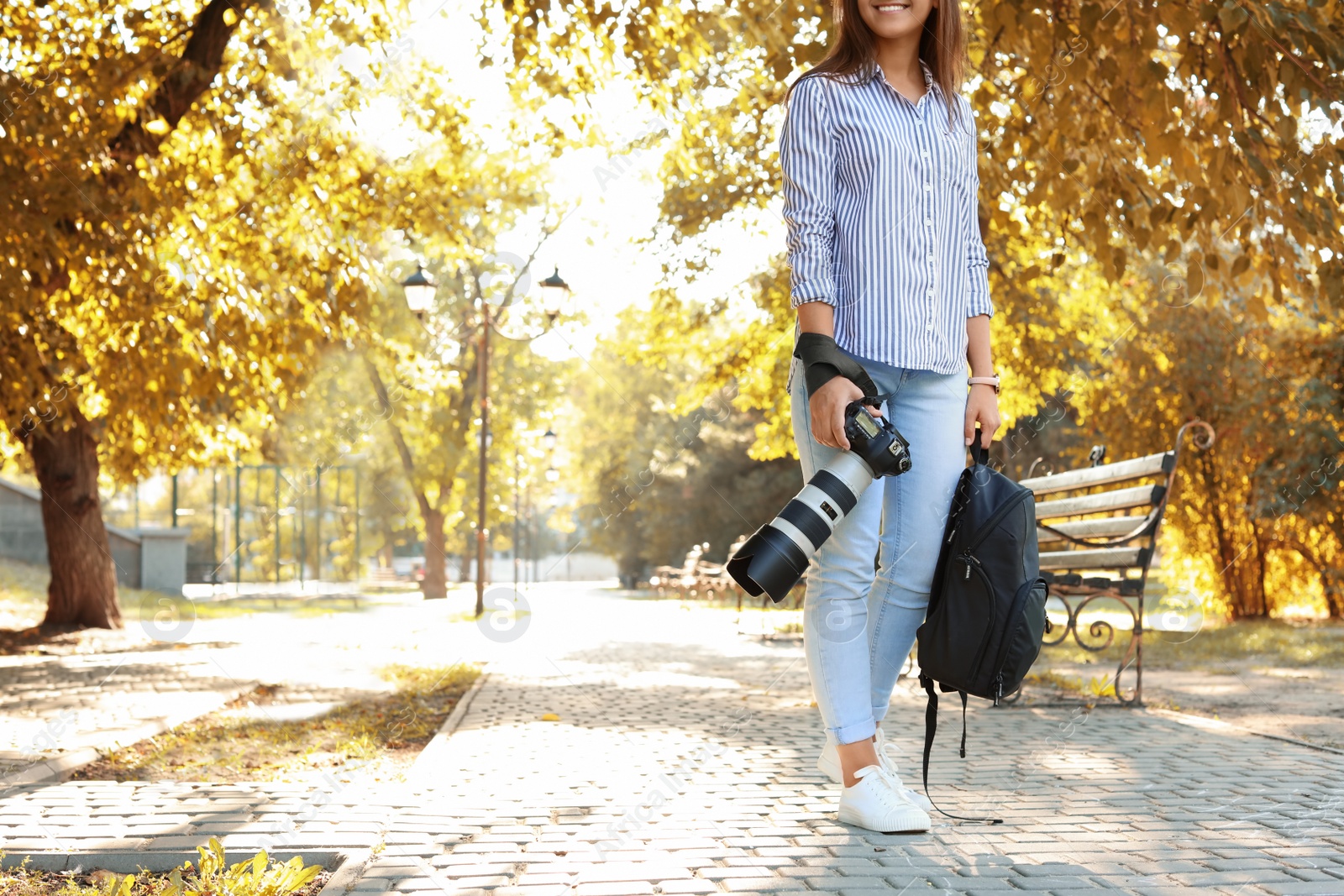 Photo of Young female photographer with professional camera and backpack in park. Space for text