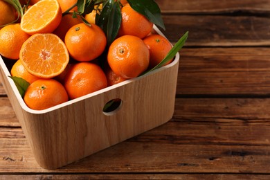 Photo of Fresh tangerines with green leaves in crate on wooden table, closeup