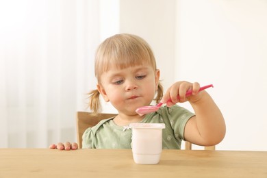 Photo of Cute little child eating tasty yogurt with spoon at wooden table indoors