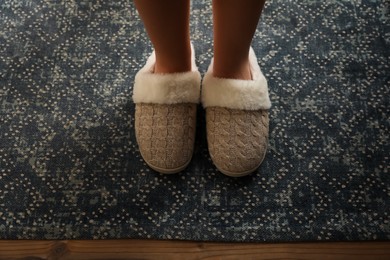 Photo of Woman wearing warm beige slippers on rug, closeup