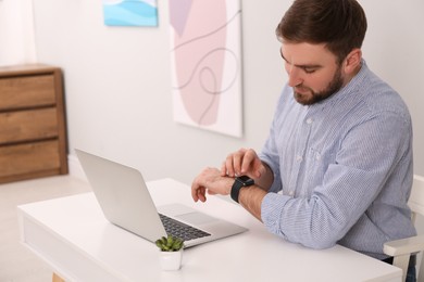 Photo of Young man using smart watch at table in office