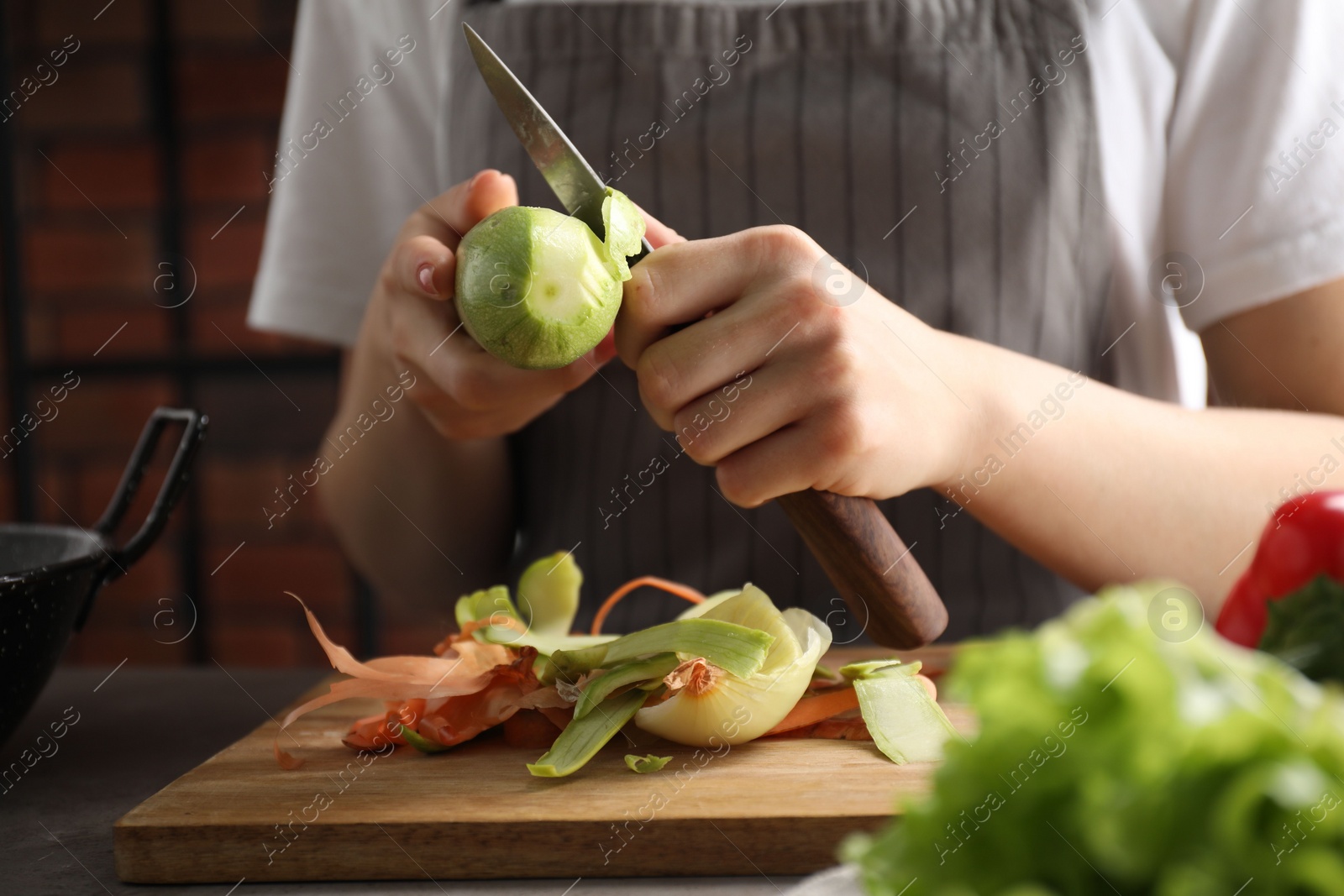 Photo of Woman peeling fresh zucchini with knife at table indoors, closeup