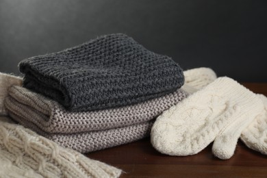 Photo of Knitted scarfs and mittens on wooden table against gray background, closeup
