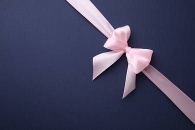 Photo of Pink satin ribbon with bow on blue background, top view. Space for text