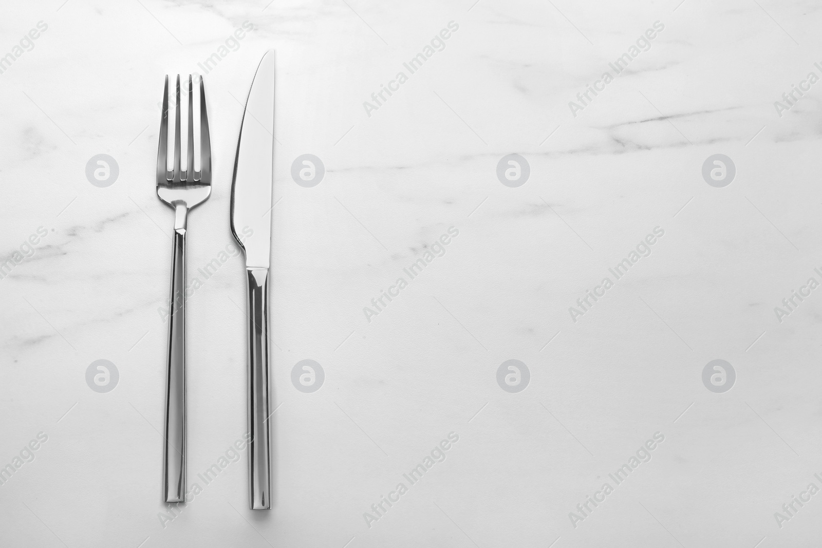 Photo of Shiny fork and knife on white marble table, flat lay. Space for text