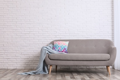 Photo of Minimalist living room interior with cozy sofa, pillow and plaid near brick wall. Space for text