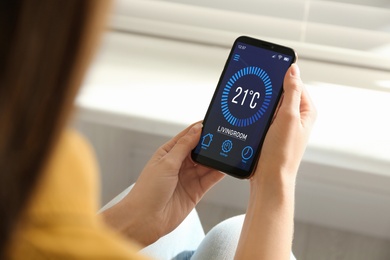 Woman using smartphone to control heating system in house, closeup