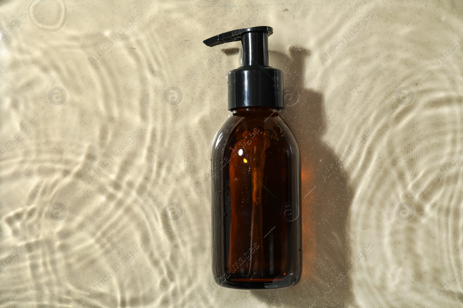 Photo of Bottle of hydrophilic oil in water on beige background, top view