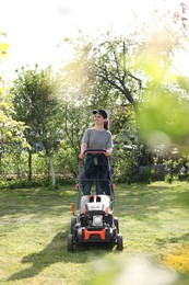 Smiling woman cutting green grass with lawn mower in garden