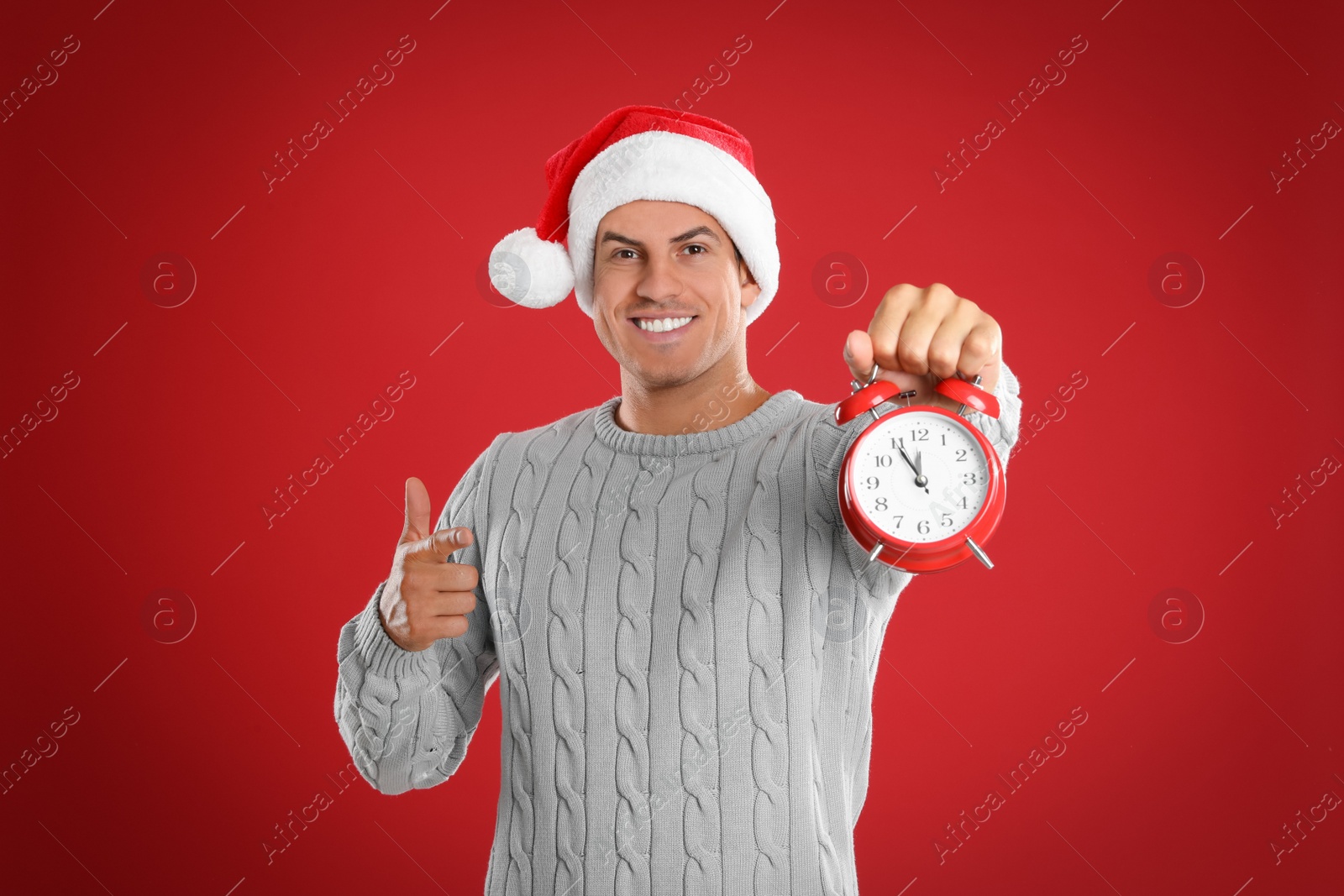 Photo of Man in Santa hat with alarm clock on red background. New Year countdown