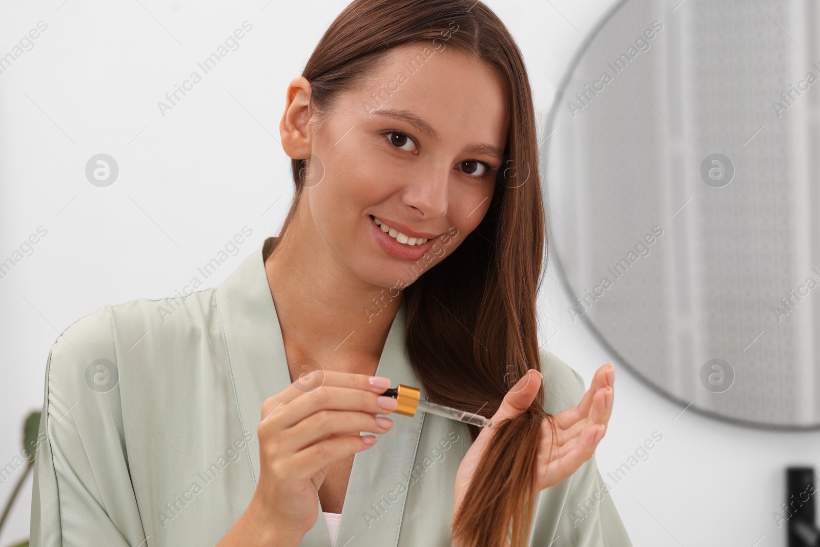 Photo of Beautiful woman applying serum onto hair indoors