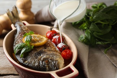 Photo of Pouring sauce into baking pan with delicious roasted dorado fish on table, closeup