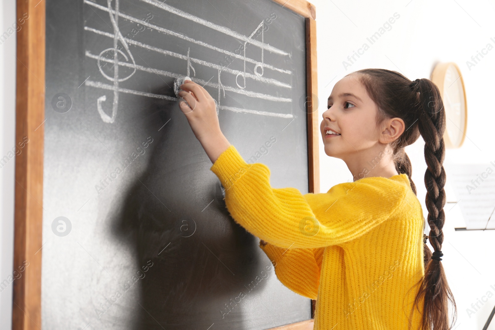 Photo of Little girl writing music notes on blackboard in classroom