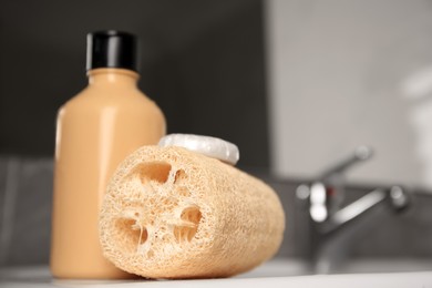 Photo of Natural loofah sponge and shower gel bottle on washbasin in bathroom, closeup. Space for text