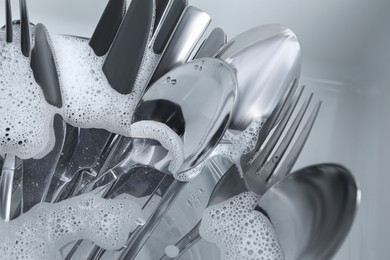 Photo of Washing silver spoons, forks and knives in foam, closeup