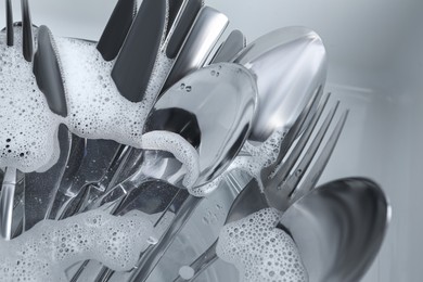 Washing silver spoons, forks and knives in foam, closeup