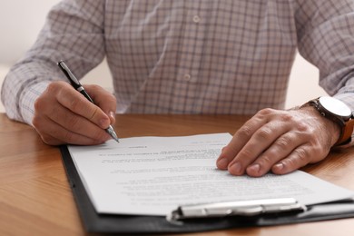 Photo of Businessman signing contract at wooden table, closeup of hands