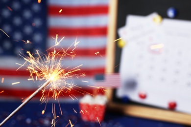 Photo of Burning sparkler against USA flag and blackboard, closeup. Happy Independence Day
