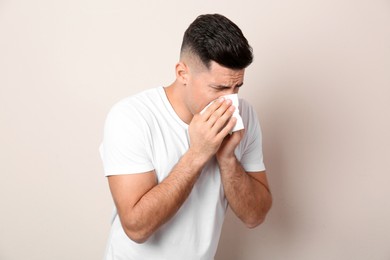 Man with tissue suffering from runny nose on beige background