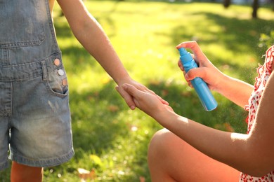 Mother applying insect repellent onto girl's hand in park, closeup