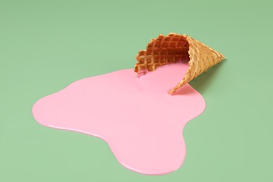 Melted ice cream and wafer cone on green background