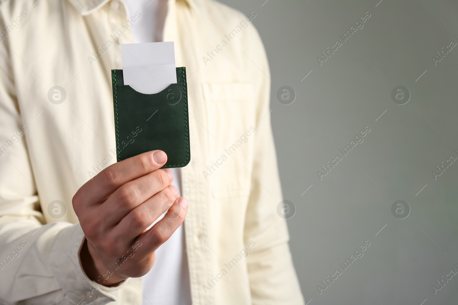 Photo of Man holding leather business card holder with cards on grey background, closeup. Space for text