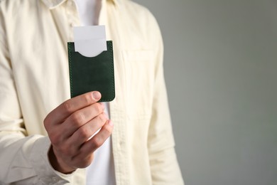 Man holding leather business card holder with cards on grey background, closeup. Space for text