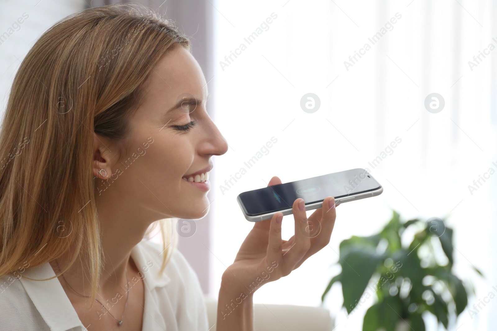 Photo of Young woman using voice search on smartphone indoors