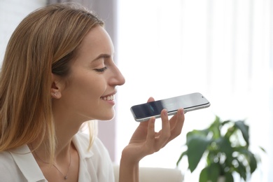Photo of Young woman using voice search on smartphone indoors
