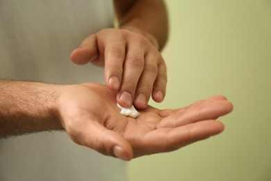 Man applying cream onto hand on green background, closeup