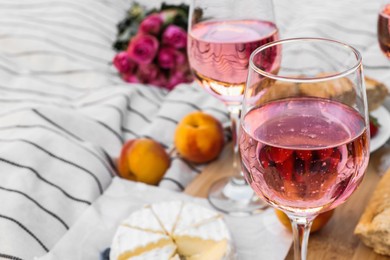 Glasses of delicious rose wine, flowers and food on white picnic blanket, closeup