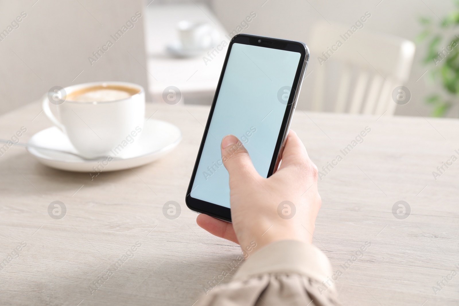 Photo of Woman with modern smartphone at white wooden table indoors, closeup