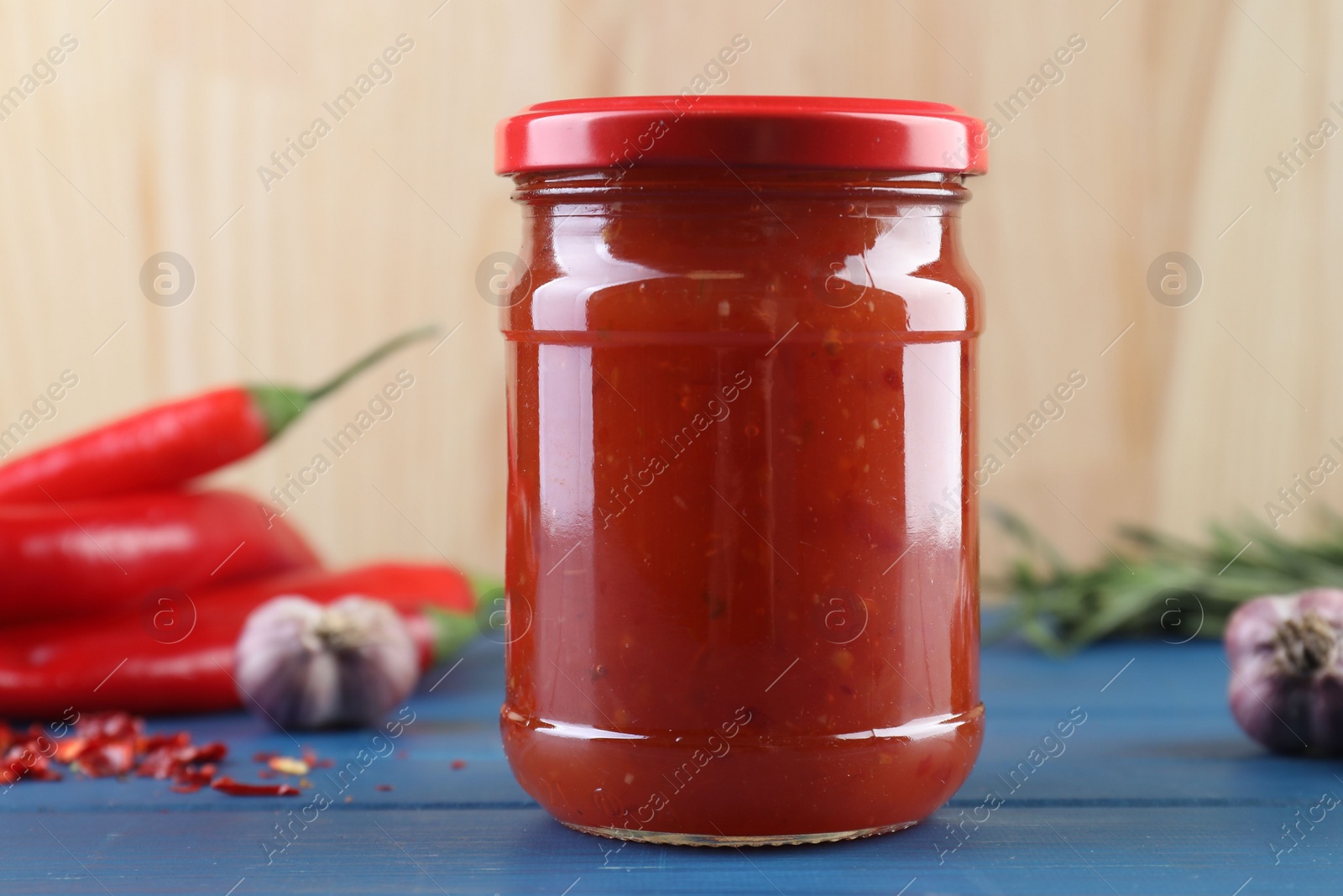 Photo of Spicy chili sauce in jar, garlic and peppers on blue wooden table, closeup