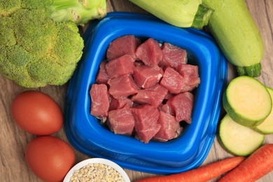 Photo of Raw meat in bowl and healthy products for pet on wooden background, flat lay