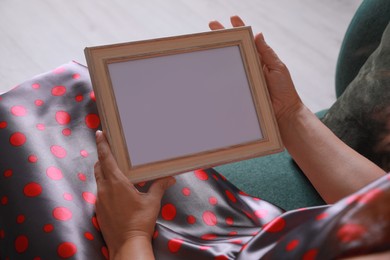 Woman holding empty photo frame indoors, closeup